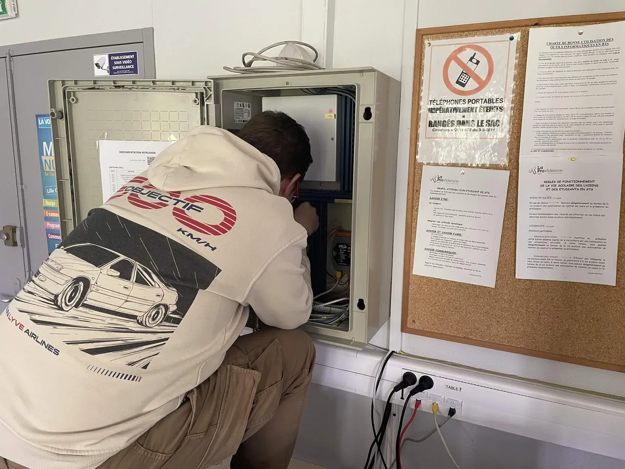 Étudiant câblant le système d'alarme et le contrôle d'accès dans l'armoire technique d'un laboratoire.